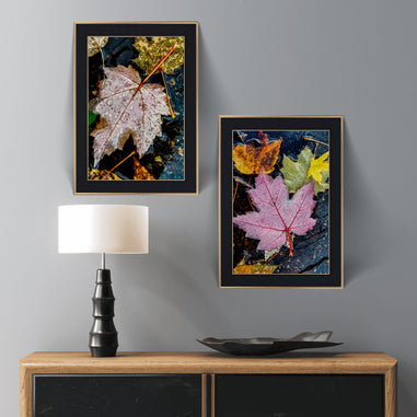 Two framed autumn leaf artworks on a gray wall above a wooden console table with a lamp and decorative bowl.