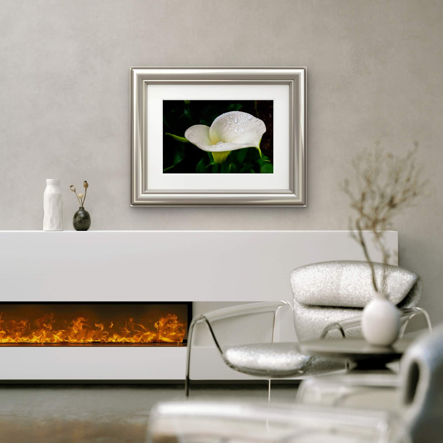 Framed artwork of a White calla lily flower with raindrops macro photography above a fireplace in a living room.
